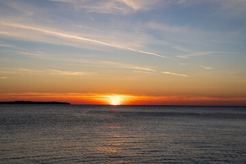 Naklejka premium Piran, Slovenia - November 3, 2024: Sunset against the backdrop of a calm sea. The sun goes down behind the sea horizon.