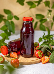 Two strawberry juice bottles standing on wooden board with fresh strawberries and leaves