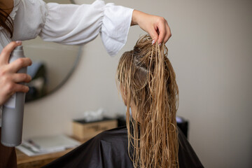 women hairdresser makes the models blonde wet hair by spraying hairspray