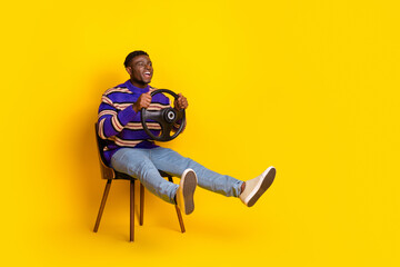 Full size photo of nice young man hold wheel sit chair empty space isolated on yellow color background
