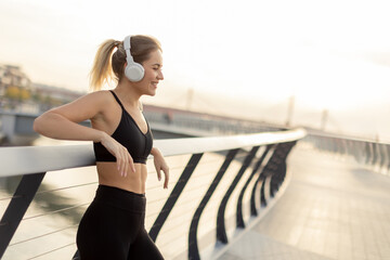 A young woman enjoys a moment of relaxation while listening to music by the riverside during the golden hour of sunset