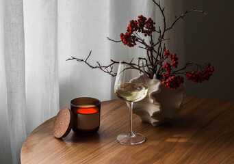 A cozy evening - a glass of white wine, a candle, an autumn bouquet on a wooden table in the living...