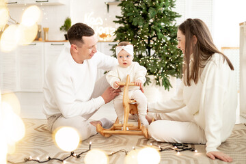 a young happy family with a small child rejoices and celebrates the New Year holiday at home in a bright room with a Christmas tree