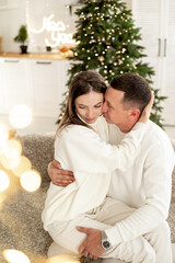 Fototapeta premium a happy young couple, a guy and a girl, kiss and hug, congratulating each other on the New Year on the background of a Christmas tree