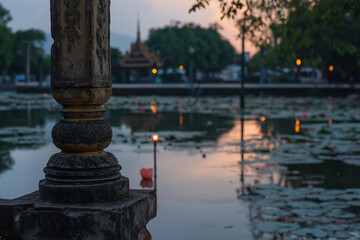 Obraz premium A stone pillar is in front of a pond with a lot of lilies. The water is calm and the sky is orange