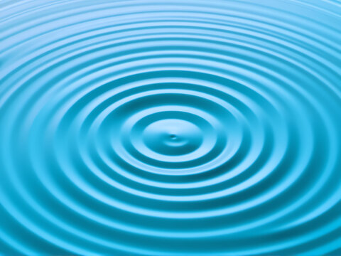 Rippling blue water surface creating circular patterns in a tranquil setting with soft light and reflections