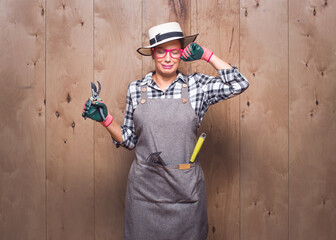 Childish gardener woman holding pruning shears crying on wooden background in studio. Funny female...