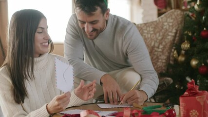 A young loving couple is writing to do list and goals on a blank paper sheet for the New Year and Christmas. 4k video