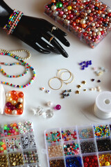 Hand figurine, colorful friendship bracelets, necklaces, various beads and DIY supplies on the table. Making jewelry at home. Selective focus.