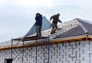 Two men are working on a roof, one of them is wearing a blue jacket