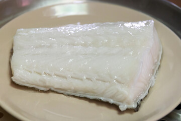 Fresh fillet of white fish on a plate, ready for cooking or serving, showcasing its smooth texture and clean appearance.