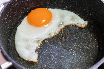 Fried egg in a pan, showcasing a rich yolk with a slightly crispy edge, perfect for breakfast or cooking inspiration.