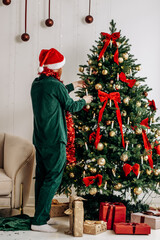 A young red-haired bearded man in the Santa Claus hat is decorating a Christmas tree at home.A New Year's concept.