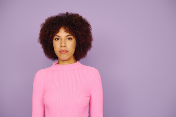 A young African American woman in casual pink attire standing against a vibrant purple backdrop.