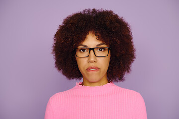 A young African American woman in pink clothing and glasses while standing on a purple backdrop.