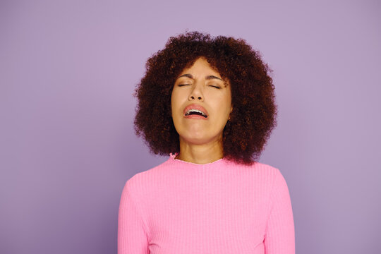 A young African American woman showcases her raw emotions, dressed in pink, with a captivating purple backdrop.