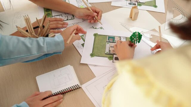 Architect and engineer use tree model discuss about building blueprint on table with architectural document, measurement tools and wooden block scatter around at modern office. Closeup. Delineation.