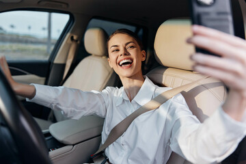 A woman is driving a car and taking a selfie with her cell phone while sitting in the driver's seat