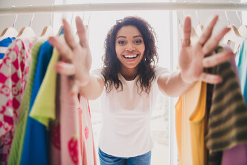Young woman with bright smile surrounded by colorful clothes in living room, showcasing shopping experience