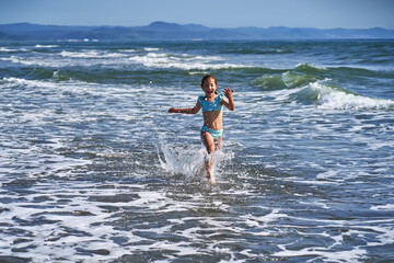 An 8 year old girl in a swimsuit having fun in the sea waves.