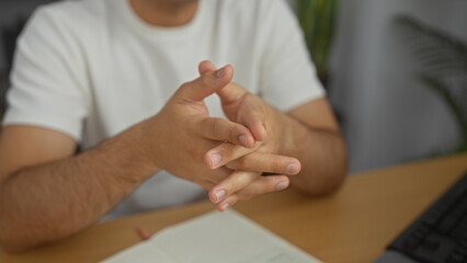 A man in an office with his hands interlocked, showcasing a focused and contemplative expression at a desk with a notebook and computer.