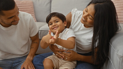 Happy hispanic family with man, woman, and child showing thumbs up while sitting together at home in a cozy living room enjoying quality time.