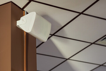 A white speaker is mounted on a brown wall