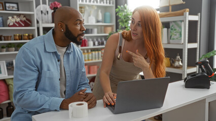 Woman pointing at laptop while talking to man in home decor store interior