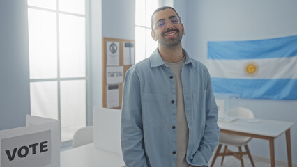 Young man smiling in an argentinian electoral college room, with a voting sign and flag in the background, exuding confidence and positivity.