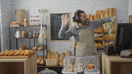 Young hispanic man with moustache dancing while working behind the counter in a bakery shop...