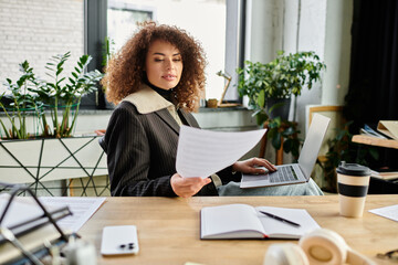 A determined woman is reading papers while seated at her desk, surrounded by plants and sunlight.