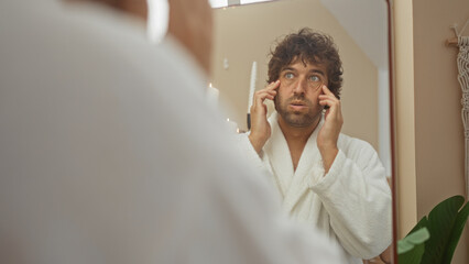 Handsome young man in bathrobe admiring himself in the mirror at a wellness spa center