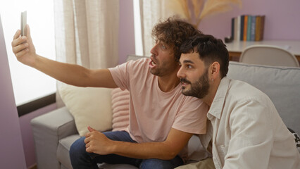 Obraz premium Men sitting together on a couch in a living room, taking a selfie with a smartphone and enjoying their time indoors, showcasing friendship and family bonds in a cozy apartment setting