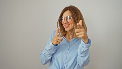 Attractive blonde woman in blue shirt smiling and pointing fingers while standing against an isolated white background