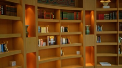 Blurred wooden bookshelves in a library setting featuring various books and soft lighting, creating a cozy and scholarly atmosphere indoors.