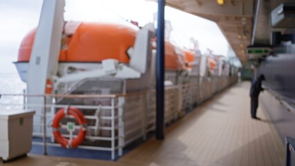 Blurred man stands on a cruise deck with lifeboats, showcasing an out-of-focus scene with bokeh lighting and a defocused ocean background for travel imagery.