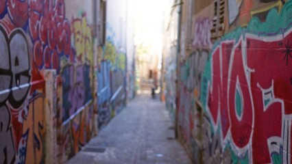 Fototapeta premium Blurred view of graffiti-covered alleyway suggests urban street art scene with vibrant colors, emphasizing defocused backgrounds typical of ghetto culture.