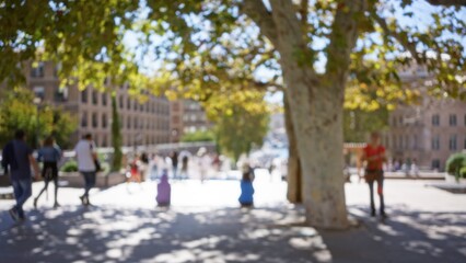 Blurred scene of people walking on a sunny street in marseilles, france with trees in the foreground creating a bokeh effect.