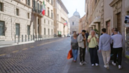 Blurred people walking on an old rome street with italian flags visible, showcasing a sunny day, defocused scene, and historic architecture, creating a casual and timeless atmosphere.