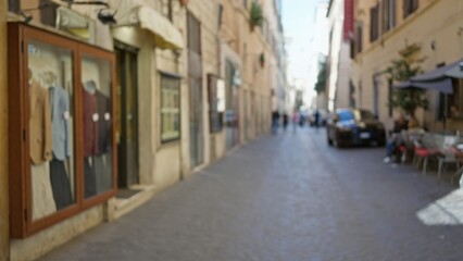Obraz premium Blurred street in rome featuring cobblestones, vintage buildings, and outdoor seating with soft bokeh effect, capturing the charming old-town ambiance.