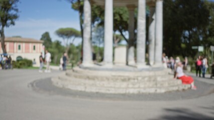 Obraz premium Blurred view of people enjoying a sunny day at villa borghese gardens, rome, with defocused columns and lush greenery in the background.