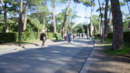 Blurred people walking in villa borghese gardens in rome with lush trees and sunshine, capturing serene outdoor vibes with defocused background and subtle bokeh effect.