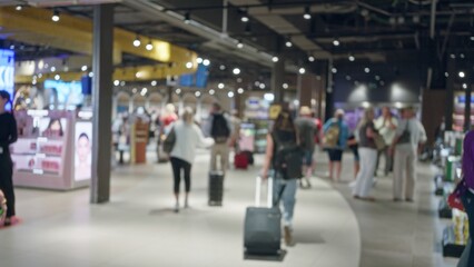 Defocused travelers with luggage in modern airport interior showcasing blurred figures under bright lights creating a bustling yet indistinct atmosphere of movement.
