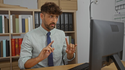 Fototapeta premium Young man having a video call in an office setting with bookshelves in the background