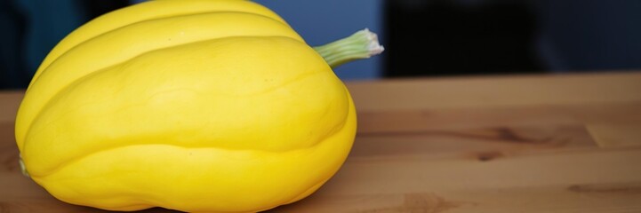 A vibrant fresh yellow pumpkin rests on a wooden table, its smooth skin slightly curved from natural drying process, nature-inspired decor, autumnal still life