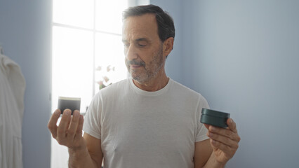Middle-aged man in a clinic room examining two containers in his hands, wearing a white shirt and looking thoughtful in a bright, serene indoor setting.