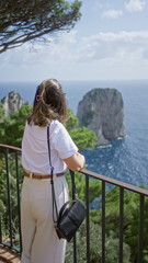 Fototapeta premium Woman gazing over scenic capri landscape with lush greenery and rock formations under a sunny sky, embodying beauty and tranquility in italy's picturesque outdoors.