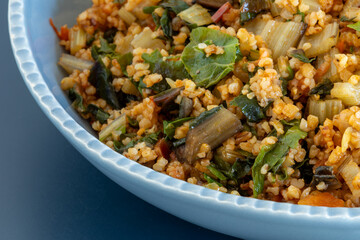 Close up view of  stove-top barley and swiss chard in blue bowl. This vegan dish is like risotto made with barley.