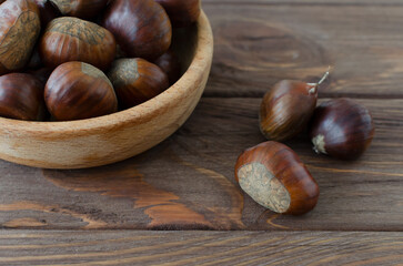 Edible raw chestnuts in a wooden bowl on the table. The concept of autumn food. Street food. Selective focus. Horizontal orientation.
