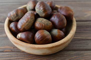 Edible raw chestnuts in a wooden bowl on the table. The concept of autumn food. Street food. Selective focus. Horizontal orientation.